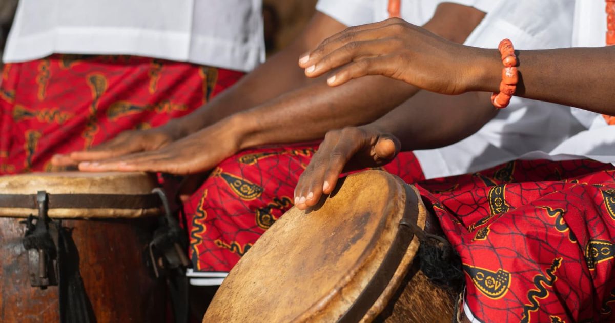 manos tocando tambores africanos tradicionales con vestimenta cultural roja e instrumentos musicales africanos