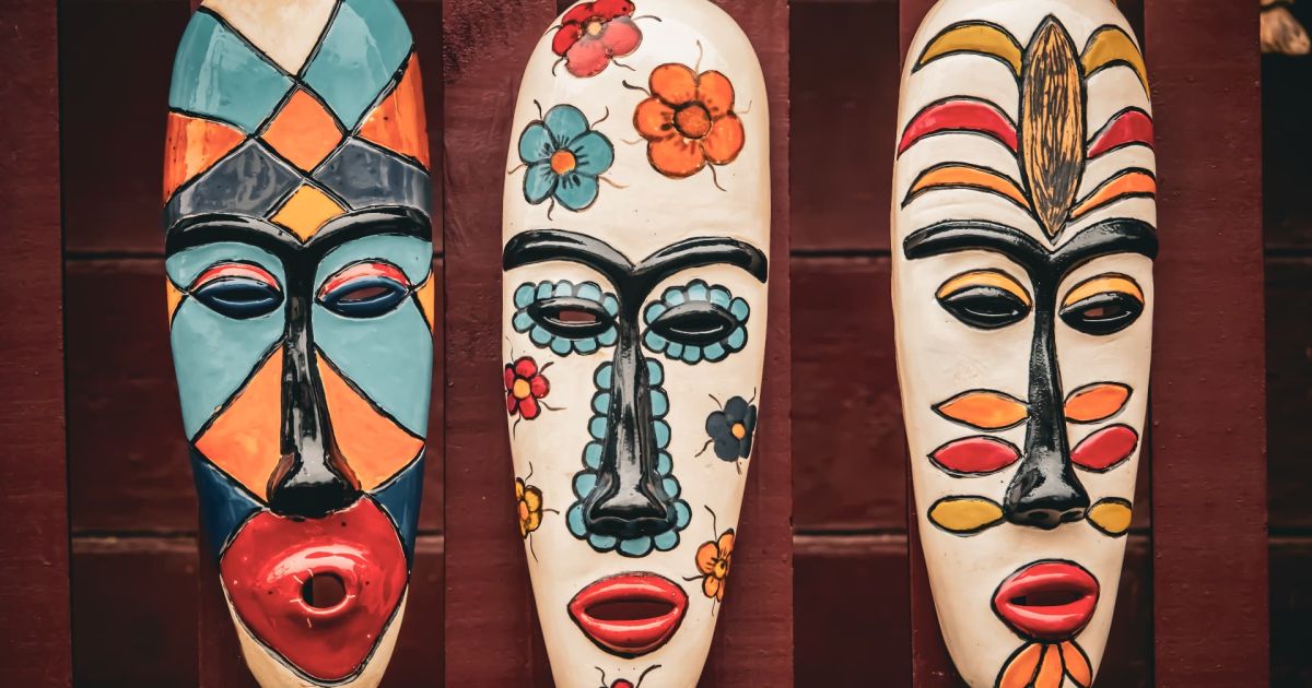Máscaras africanas decorativas colgadas en una pared de madera, elaboradas artesanalmente y pintadas a mano con colores intensos, patrones geométricos y motivos florales de inspiración cultural africana