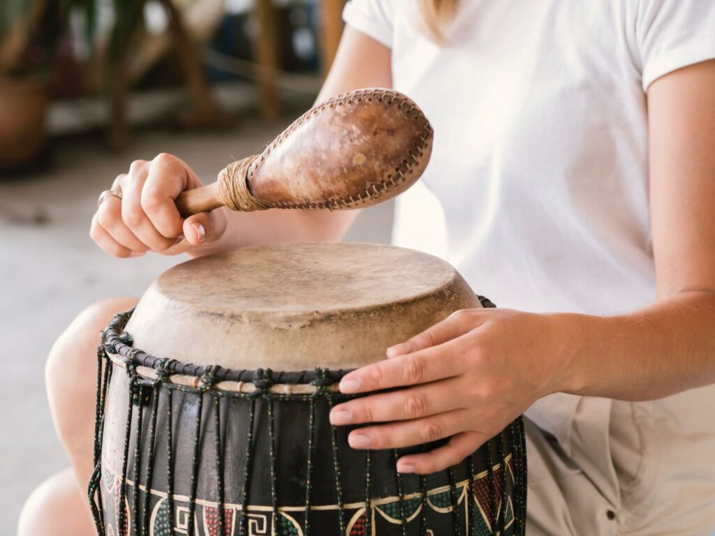 persona tocando un instrumento de percusión africano con tambor djembe y maraca artesanal en primer plano