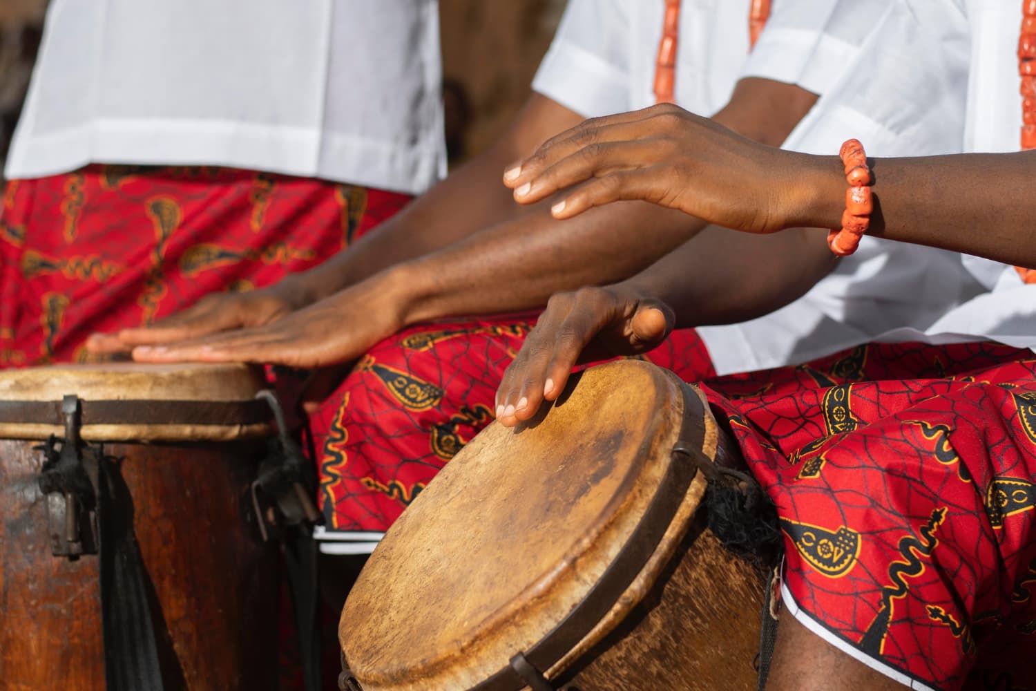 manos tocando tambores africanos tradicionales con vestimenta cultural roja e instrumentos musicales africanos