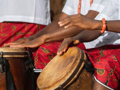 manos tocando tambores africanos tradicionales con vestimenta cultural roja e instrumentos musicales africanos